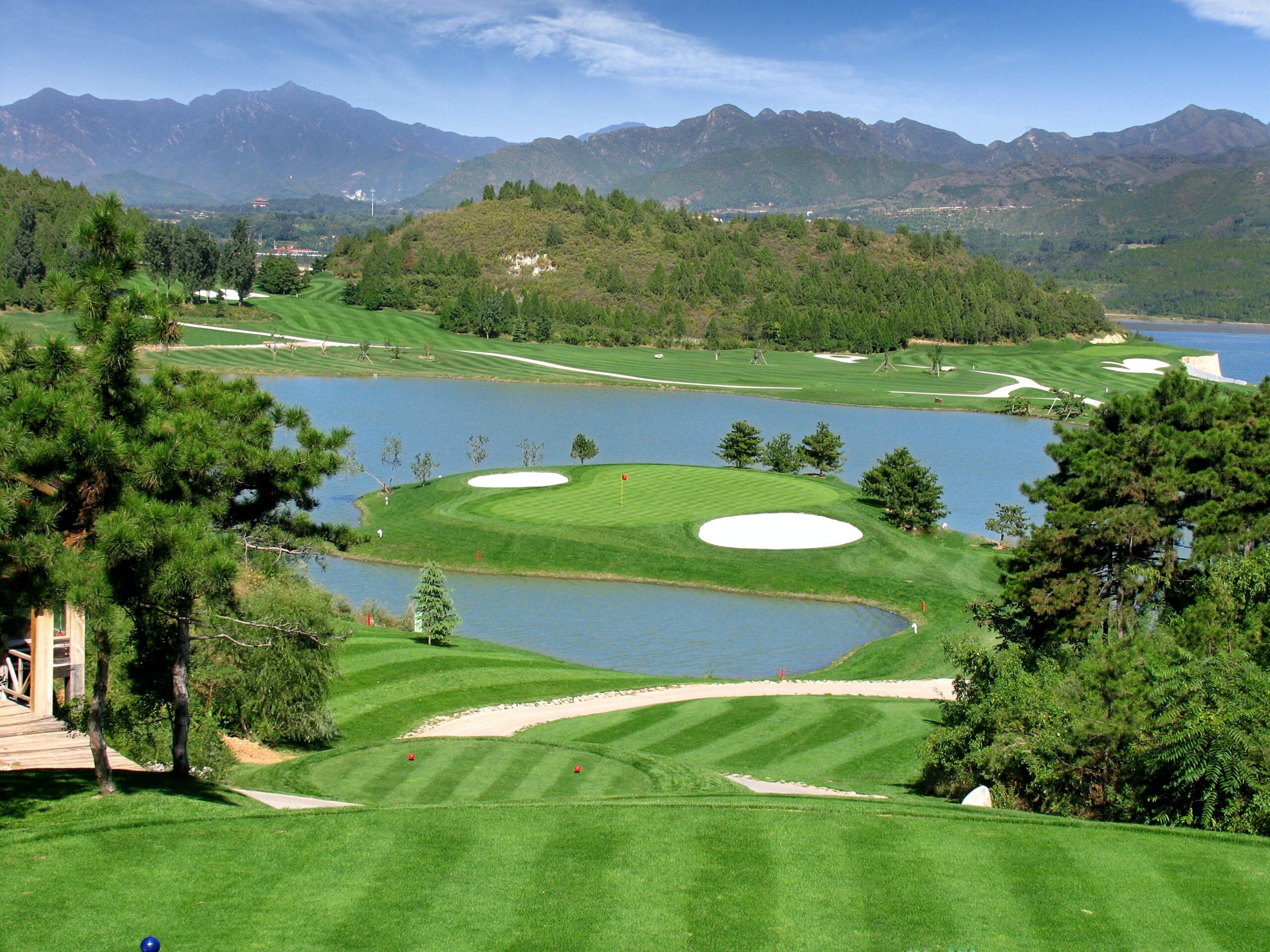 View of a golf green below surrounded with water with a mountain backdrop